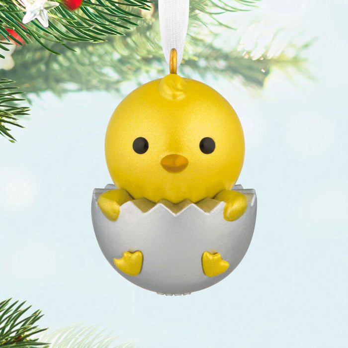 Yellow chick in an eggshell Christmas ornament on a tree branch.