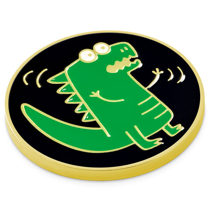 A round enamel pin featuring a green cartoon dinosaur on a black background with a gold border, shown on a plain white background.