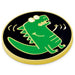 A round enamel pin featuring a green cartoon dinosaur on a black background with a gold border, shown on a plain white background.