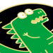 A close-up of a green cartoon dinosaur enamel pin with gold outlines on a black background.