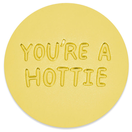 A round yellow coaster with the phrase 'YOU'RE A HOTTIE' embossed in raised letters, shown on a clean white background.
