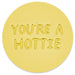 A round yellow coaster with the phrase 'YOU'RE A HOTTIE' embossed in raised letters, shown on a clean white background.