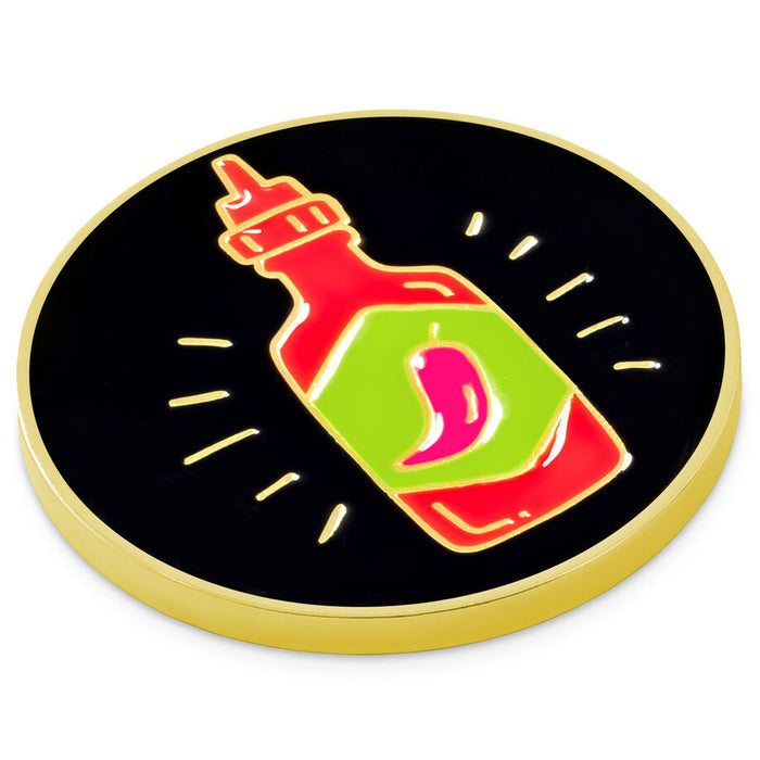 A round enamel pin featuring a stylized hot sauce bottle with a red body, green label, pink chili pepper, and a gold-tone border on a black background.