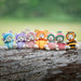 Colorful teddy bear figurines in various costumes on a wooden log with a green blurred background