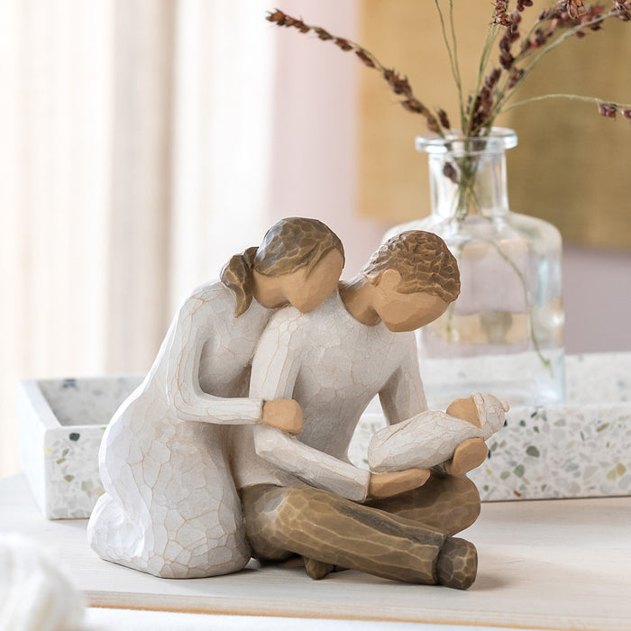Decorative figurine of a woman holding a child on a table with a vase in the background