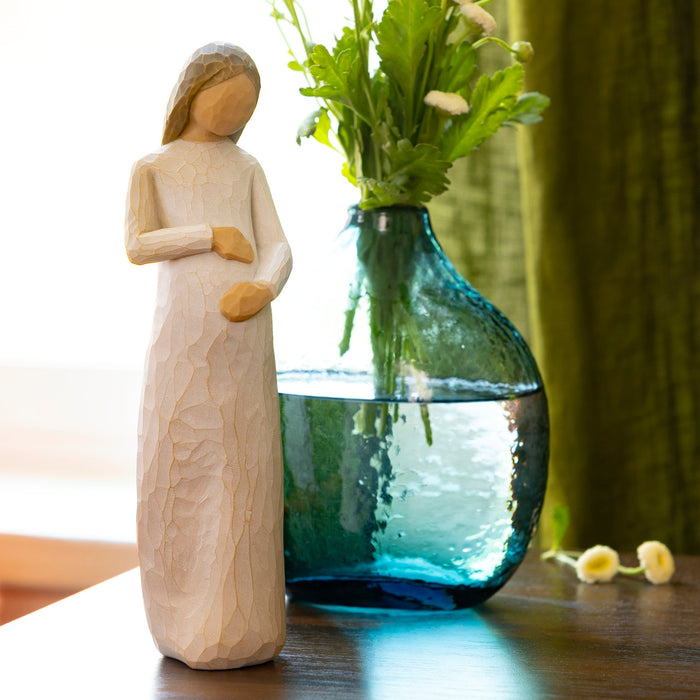 Wooden figurine of a woman next to a blue vase with flowers on a wooden surface.