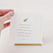 Hand holding a small white card with a motivational quote and a green leaf design on a light background.