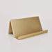 A minimalist gold metal tabletop organizer with a triangular stand and a curved horizontal bar, shown on a clean white background.