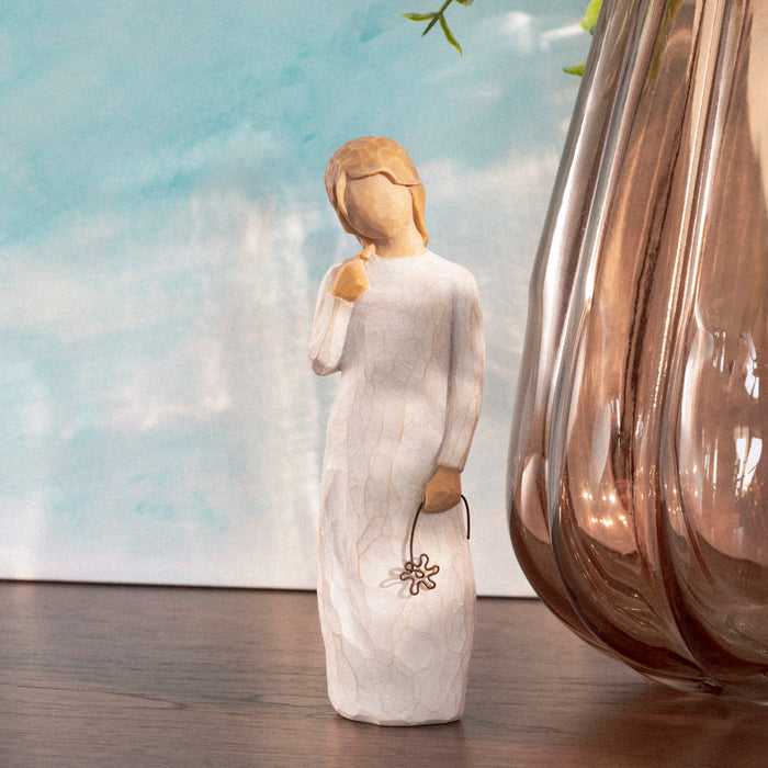 Statue of a woman holding a flower with a glass vase in the background