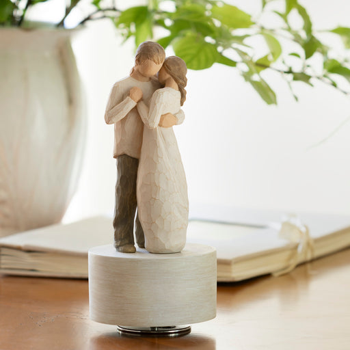 Statue of a couple embracing on a wooden base with a blurred indoor background