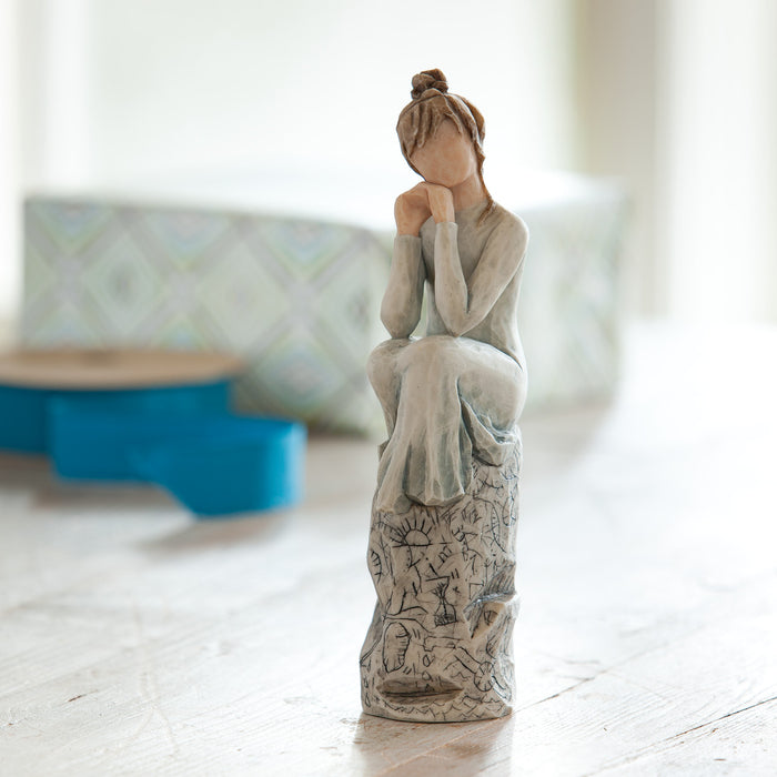 Statue of a woman sitting with her hands on her head on a wooden floor.
