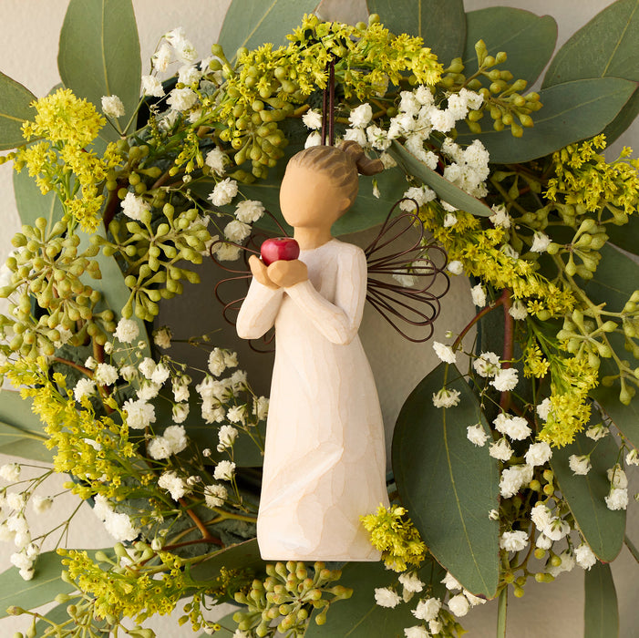 Decorative wreath with greenery and a small figurine holding apples.