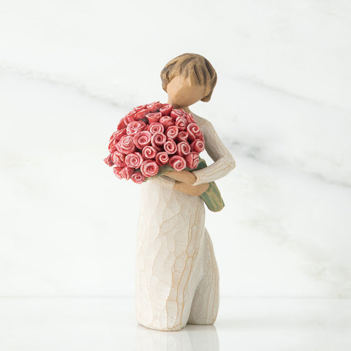 Standing figure in cream dress holding large bouquet of pink roses