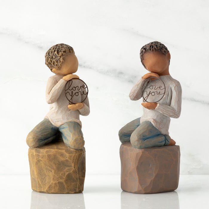 Two figurines of children holding 'I love you' signs on a white background