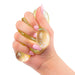A hand with pink manicured nails squeezing a translucent, glittery gold stress toy against a solid white background.
