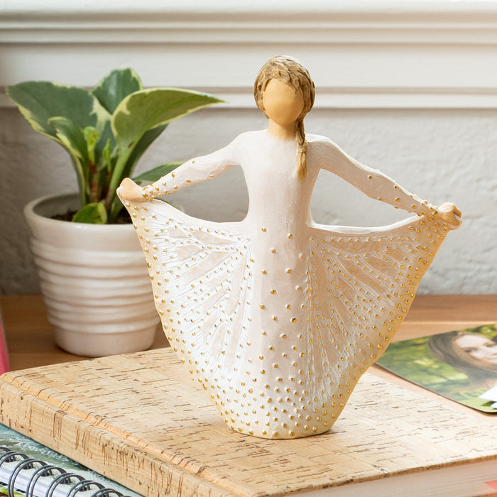Standing figure in cream dress, holding the sides of her skirt out with both hands. Skirt has carved markings of a monarch butterfly, dotted with gold leaf