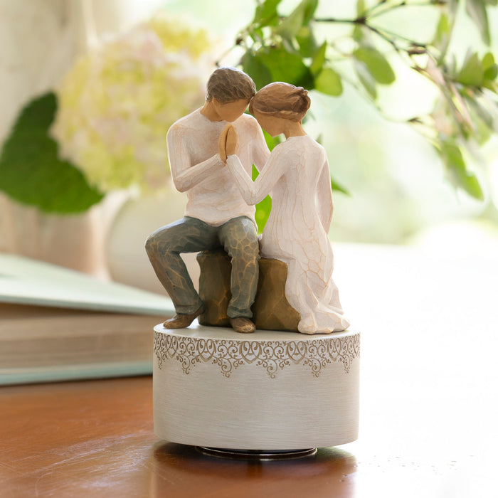 Statue of a couple sitting together on a decorative base with a blurred floral background