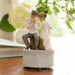Statue of a couple sitting together on a decorative base with a blurred floral background