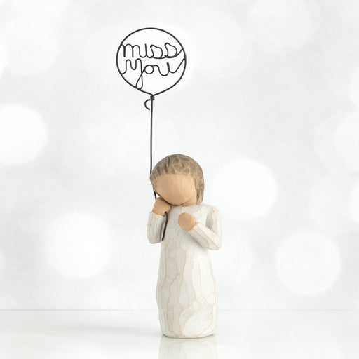 White figurine holding a balloon with 'miss you' text on a white background