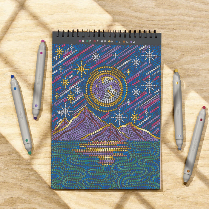 Decorative notebook with celestial design on a wooden surface with dot markers.