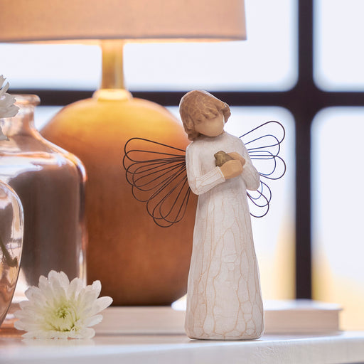 Decorative angel figurine with wings holding a bird, placed on a surface with a blurred background.