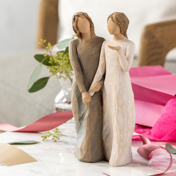 Two figurines of a couple holding hands on a decorative surface with flowers and ribbons.