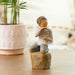 Decorative figurine of a child holding a heart with 'love you' on a wooden base, placed on a surface with a blurred background.