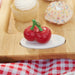 Decorative cherry on a white base with a wooden surface and pastries in the background.