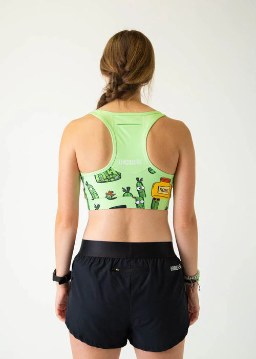 Person wearing a green sports bra with cactus design and black shorts on a white background