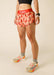 Person wearing pink shorts with chili pepper pattern and red waistband on a beige background