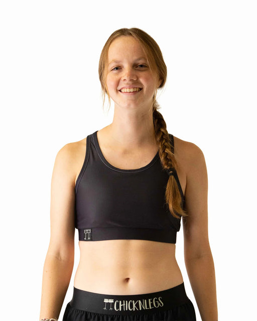 Woman wearing a black sports bra and shorts with 'CHICKNLEGS' branding on a white background