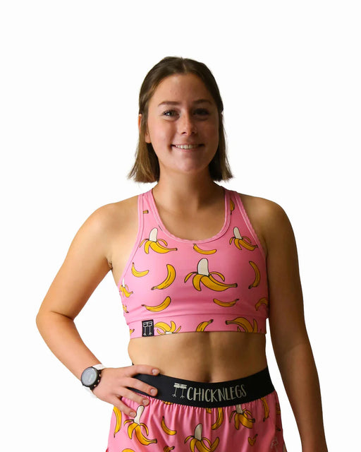 Person wearing a pink sports bra and shorts with banana pattern, holding a black belt.