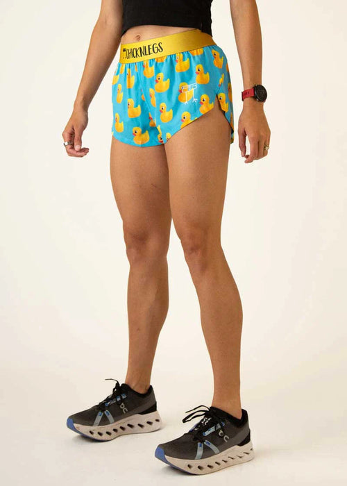 Person wearing blue shorts with rubber duck pattern and black sneakers on a white background
