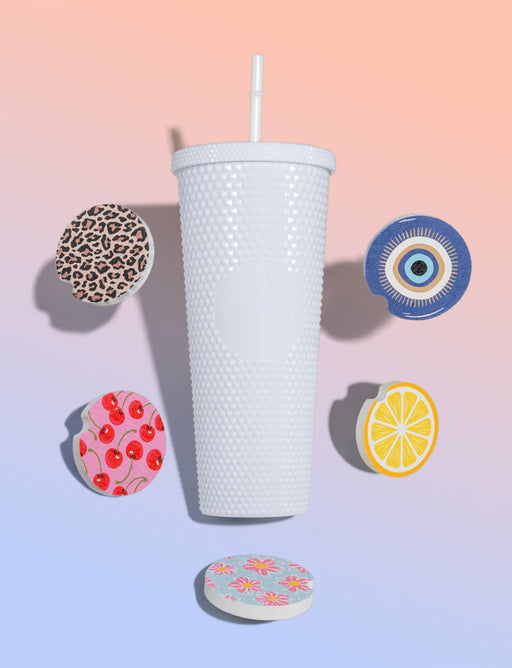 White textured tumbler with a straw on a gradient pink to blue background with colorful coasters.