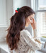 Woman with a decorative hair clip in her hair, wearing a polka dot sweater, standing by a window.