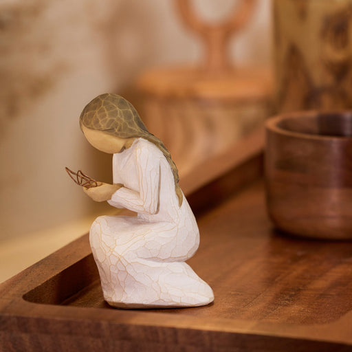 White figurine of a woman holding a butterfly on a wooden surface