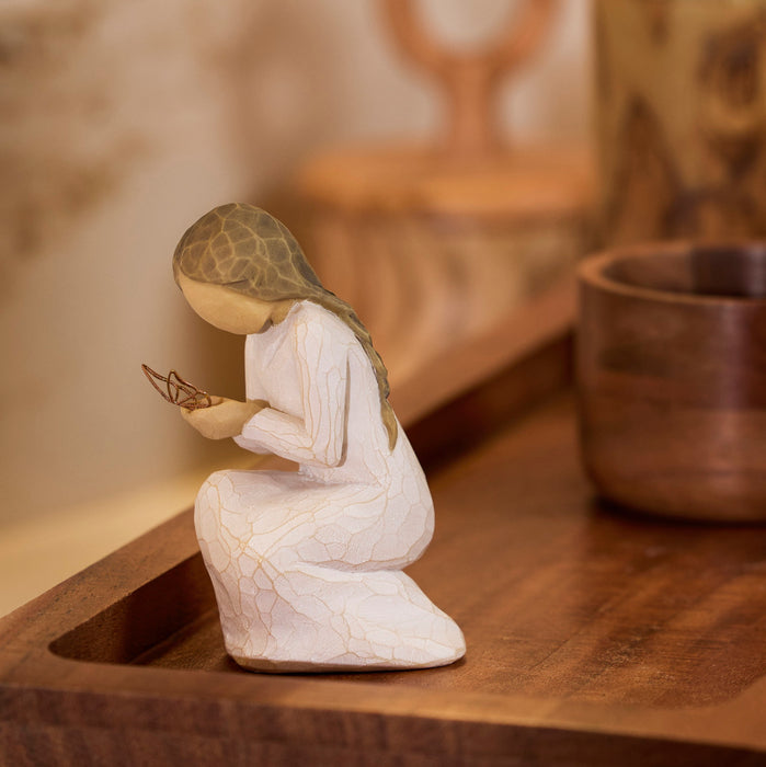 White figurine of a woman holding a butterfly on a wooden surface