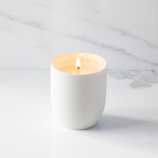 White candle in a ceramic holder on a marble surface