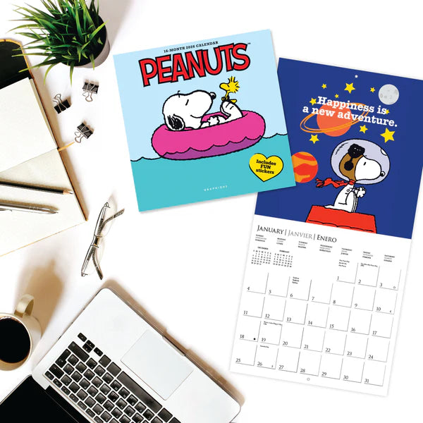 Two Peanuts-themed calendars on a desk with a laptop and coffee cup.