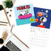Two Peanuts-themed calendars on a desk with a laptop and coffee cup.