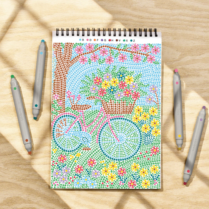 Coloring book with a bicycle and flower design on a wooden surface with coloring pencils.
