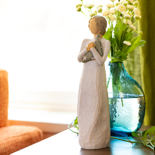 Decorative figurine of a woman holding flowers next to a blue vase with greenery on a table.
