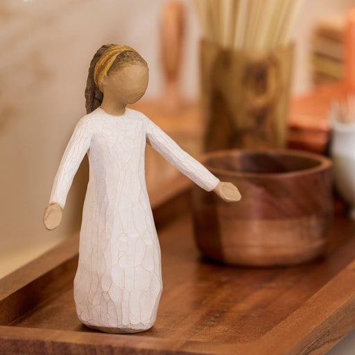 Wooden figurine of a woman in a white dress on a wooden surface with blurred background