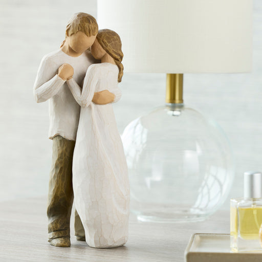 Statue of a couple embracing on a surface with a lamp and perfume bottle in the background.