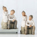 Two sets of figurines of children sitting on stools against a white background