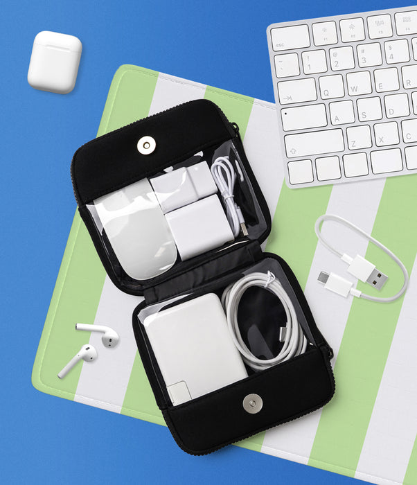An open black zippered electronics accessory organizer bag displayed on a green and white striped surface, surrounded by a keyboard, earbuds, a charging case, and cables on a blue background.