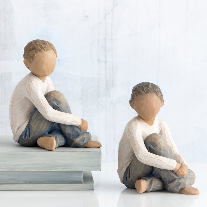 Two figurines of children sitting on a bench against a light background