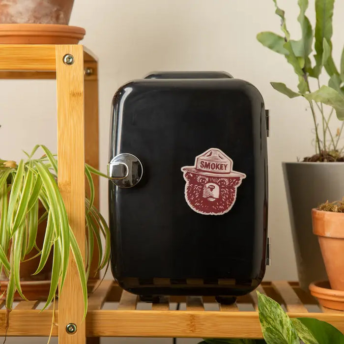 Black mini refrigerator with Smokey Bear logo on a wooden shelf with plants