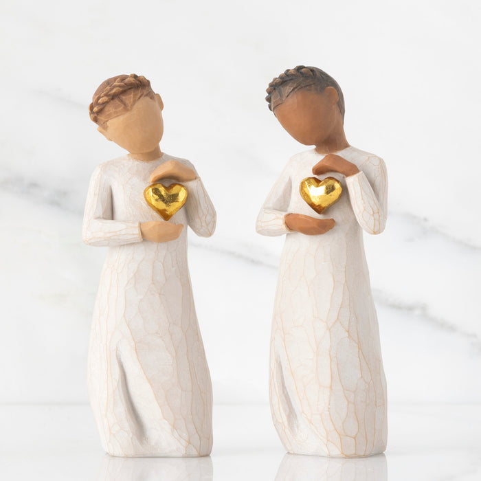 Two figurines holding gold hearts against a white background