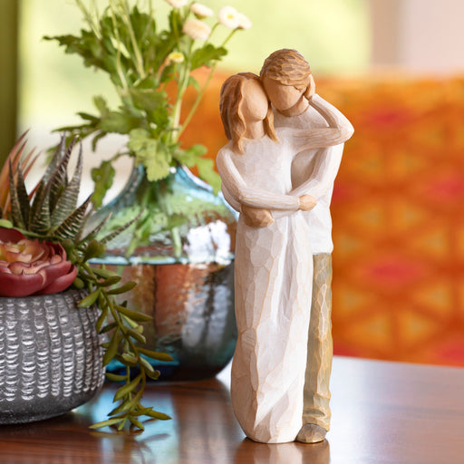 Figure of couple, standing with arms around each other. Woman in cream dress, with lighter skin tone and hair color, man in cream shirt and dark pants with lighter skin tone and hair color